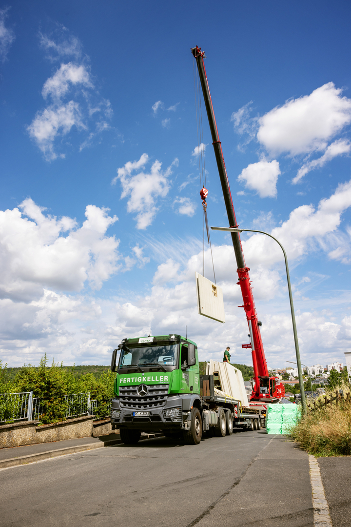 Kran hebt Betonwand von LKW auf Baustelle